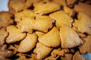 A close-up view of a pile of golden brown gingerbread cookies in various festive shapes, including bells and stars. Their rustic texture creates a cozy, homemade feel.