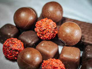 A detailed close-up of chocolate truffles featuring bright red chips surrounded by smooth chocolate balls and square shapes. Perfect for holiday or dessert themes.