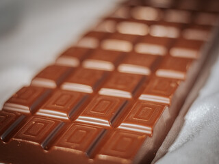 A milk chocolate bar with a geometric square pattern photographed with a soft focus effect against a light fabric background. Perfect for confectionery and dessert themes.