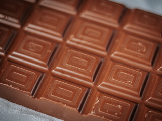 A milk chocolate bar with a geometric square pattern photographed with a soft focus effect against a light fabric background. Perfect for confectionery and dessert themes.