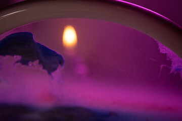 A soft orange flame glows against a dreamy pink and purple ambient background with textured organic...