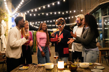 Friends celebrating birthday party at night with gift and drinks