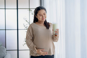 Asian female pregnant holding glass of milk in the living room, self care