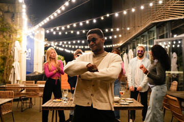 Young man dancing with friends at outdoor party under string lights