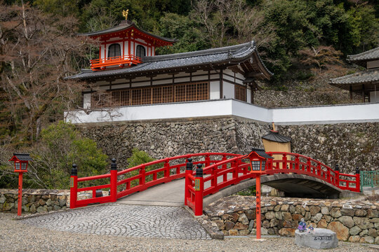 A picturesque Japanese temple nestled on a hillside, featuring a vibrant red bridge in Minoh National Park, Osaka, Japan. It evokes the serenity of ancient Buddhist practices.