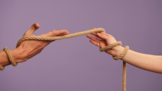 Man and woman hands tied together, tangled with rope, abusive or codependent relationships concept, isolated on purple studio background, close up shot.