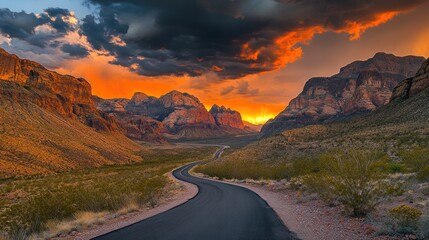 Dramatic sunset over winding desert road in mountainous canyon.