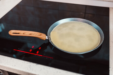 Cooking Crepe Batter on a Nonstick Pan with Wooden Handle on a Modern Induction Stove