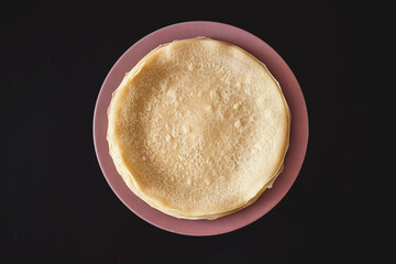 Stack of Freshly Cooked Crepes on a Red and White Striped Plate Against a Black Background