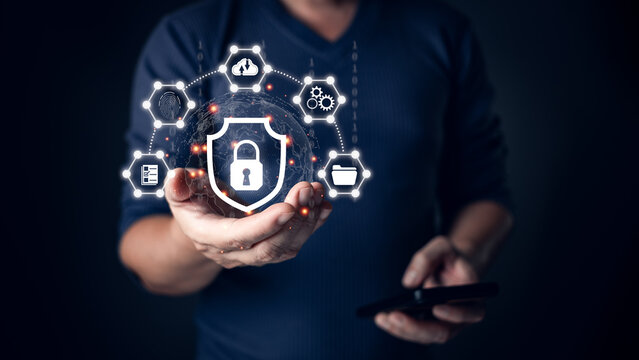 A person holding a glowing shield icon symbolizing cyber security, surrounded by connected digital icons representing data protection, secure networks, and technology safeguards in a dark setting.