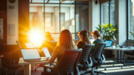 A brightly lit office with several people working at laptops. The sun shines from behind, creating a warm, inviting atmosphere
