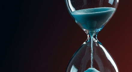 Hourglass with blue sand flowing against a dark background