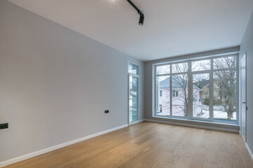 An empty room, unfurnished in a country house, with a fine finish. Panoramic Windows with a view of the winter landscape and nearby houses.