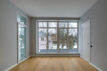 A room with a final finish, unfurnished, in a country house. Glass door, panoramic window with a view of the winter landscape.