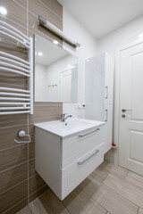 Modern Home Bathroom Interior with Sink, Mirror, and Stylish Tiled Walls. Heater on the Wall. Closed Wooden Door
