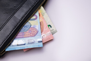 Black leather wallet with five, ten and twenty euro bills banknotes on white background 