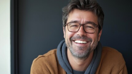 Obraz premium Smiling adult man with glasses and facial hair laughing at the camera against a clean dark background, wearing casual clothing and a jacket