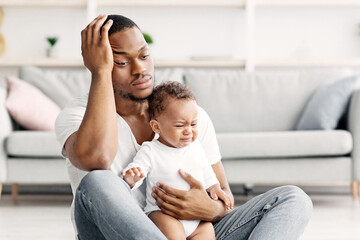 Daddy Blues. Stressed Young Black Father Sitting With Crying Infant Baby On Floor At Home,...