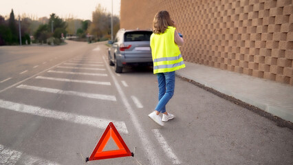 Woman requesting help by cell phone for broken down car and breakdown triangle