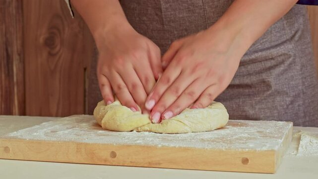 Female hands kneading the dough on wooden board with flour