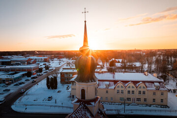 A church with an onion shaped dome and cross glows in sunset light, surrounded by snow covered buildings, streets, and a mix of trees and structures.