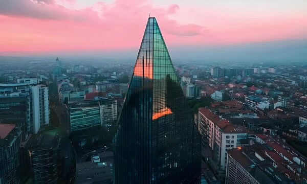 Modern Glass Skyscraper Reflecting Sunset Glow Above Urban Cityscape with Pink Sky and Buildings in the Background