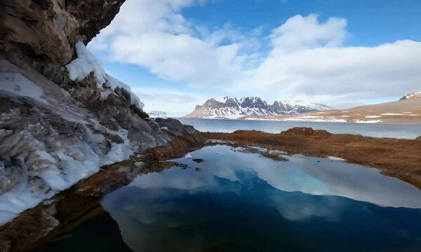 Scenic Arctic Landscape with Snowy Mountains, Frozen Lake Reflection, and Rocky Foreground Under Clear Blue Sky