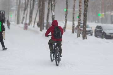 A cyclist rides along a snowy road in the city. Heavy snowfall.