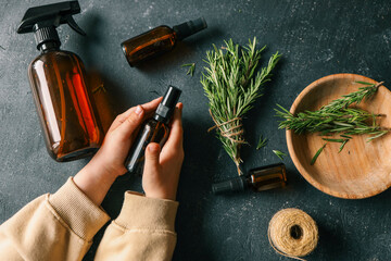 Amber glass spray bottle with a black cap placed on a dark rustic surface, surrounded by rosemary...