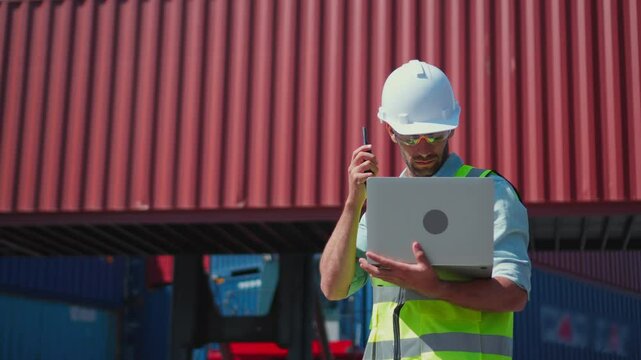 Caucasian male custom clearance officer checking the imported cargo at container yard. The officer is checking while using laptop and walkie-talkie for import and export shipment at container yard.