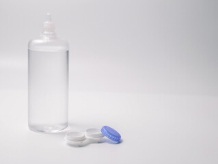 Transparent contact lens solution bottle and open lens case with blue lid on white background....