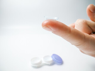 Close-up of a transparent contact lens balanced on a fingertip against a white background. Concept of eye care, vision correction, optical clarity, and hygiene