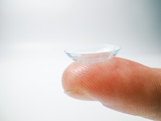 Close-up of a transparent contact lens balanced on a fingertip against a white background. Concept of eye care, vision correction, optical clarity, and hygiene