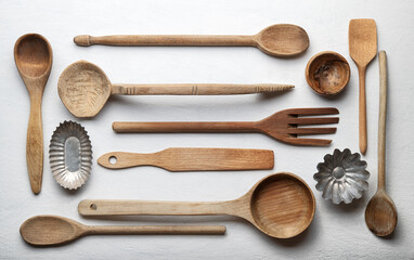 Ladles and other wooden kitchen tools on white roughcast background, top view