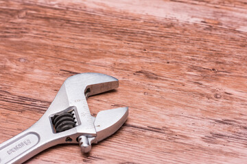 Silver adjustable wrench lying on a wooden surface. The wrench is open, suggesting recent use. The...