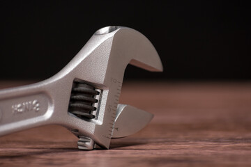 Silver adjustable wrench with a black handle sits on a wooden surface. The wrench is marked with...
