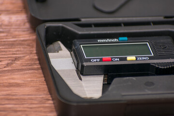 Fototapeta premium Digital caliper lies in a black case on a wooden surface, featuring a black and silver design with a clear digital screen. Combination of precise engineering and natural wood creates visual contrast