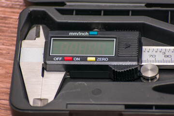 Obraz premium Digital caliper lies in a black case on a wooden surface, featuring a black and silver design with a clear digital screen. Combination of precise engineering and natural wood creates visual contrast