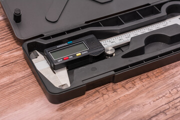 Obraz premium Digital caliper lies in a black case on a wooden surface, featuring a black and silver design with a clear digital screen. Combination of precise engineering and natural wood creates visual contrast