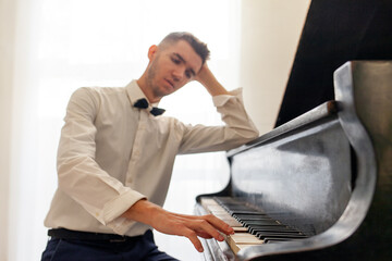 young guy in white shirt plays on old black piano, musician pianist performs melody on acoustic...