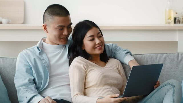 A young couple sits comfortably on a couch, sharing a delightful moment as they look at a laptop together. The cozy atmosphere enhances their connection and joy.