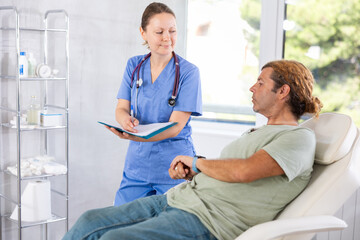 Fototapeta premium Adult female doctor in medical uniform signing contract with adult male patient in medical room