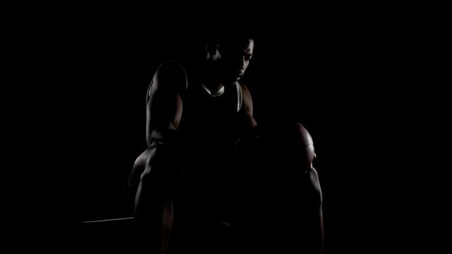 Basketball player sitting on a bench. Concentrated african american sports man against black background.