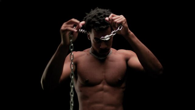 Muscular man showing muscles and holding a chain. African American male posing against black background.