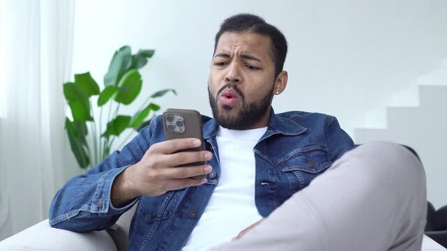 shocked african american man using smartphone at home and surprised, excited guy looking at phone and typing online in amazement