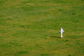 Lone figure in protective gear walking in a vast green field under a clear sky