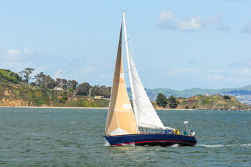 Obraz premium Sailboat gliding on scenic San Francisco Bay with hills and bright sky.