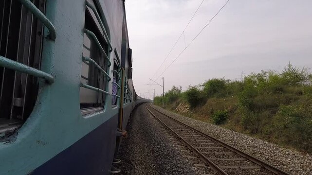POV or first hand view of a train in india. Camera out of the train rolling next to indian train on double track. Traditional blue carriages, speeding on the tracks