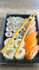 Appetizing Japanese Sushi box set served in a black plastic tray with transparent lid. Healthy Japanese Asian cuisine. Home delivery concept, Sushi to go. Vertical photo