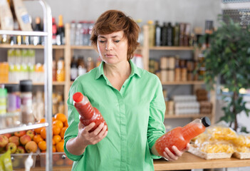 Woman hold packages bottles and choose consider juice in store. Market visitor choose consider make...
